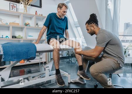 Männlicher Physiotherapeut, der das Knie des Patienten in der Praxis auscheckte Stockfoto