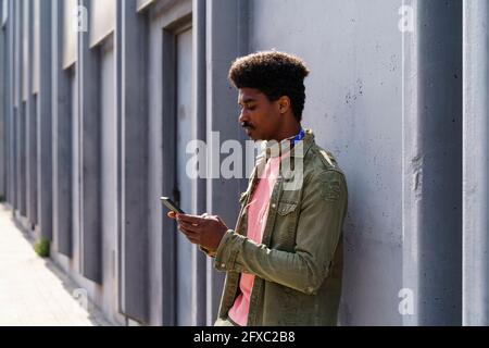 Mann mit mittlerem Erwachsenenalter, der Smartphone benutzt, während er sich an die Wand lehnt Stockfoto