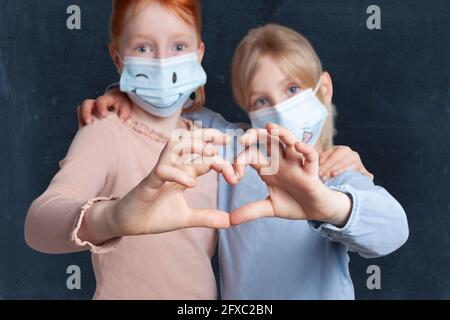 Schwestern machen Herzform mit Händen tragen Gesichtsmaske vor schwarzem Hintergrund Stockfoto