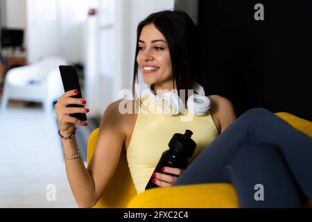 Lächelnde Sportlerin mit Mobiltelefon, während sie auf einem Sessel sitzt Stockfoto