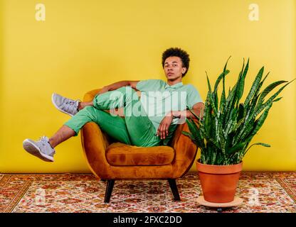 Junger Mann, der auf einem Sessel an einem Werk sitzt Stockfoto