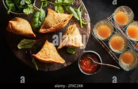 Untersetzer mit Samosa-Knödeln, Rucola-Salat, Schüssel mit Chilisauce und Gläsern Chai-Tee Stockfoto
