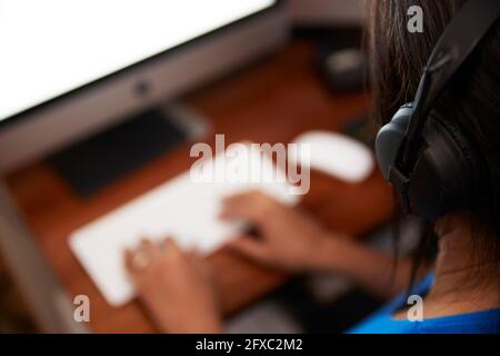 Frau mit Kopfhörern, die zu Hause am Computer arbeitet Stockfoto