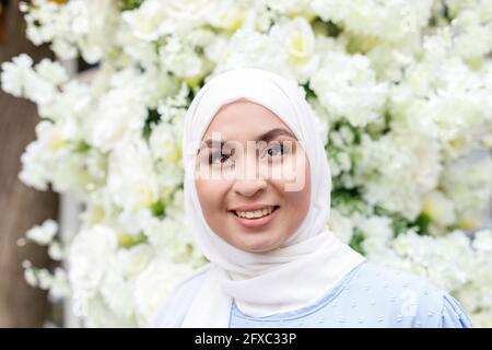 Schöne Frau mit Hijab vor weißen Blumen Stockfoto