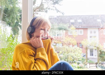 Reife Frau mit geschlossenen Augen, die zu Hause Musik über Kopfhörer hört Stockfoto