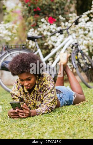 Frau, die im Garten auf Gras liegt und ein Mobiltelefon benutzt Stockfoto