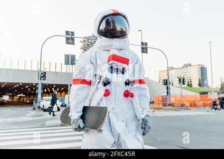 Männlicher Astronaut mit Skateboard auf dem Crosswalk in der Stadt Stockfoto