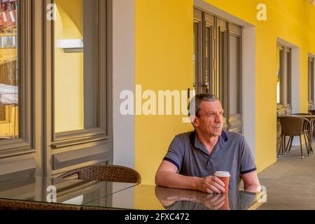 Ein erwachsener älterer Mann sitzt an einem Tisch und trinkt Kaffee Stockfoto