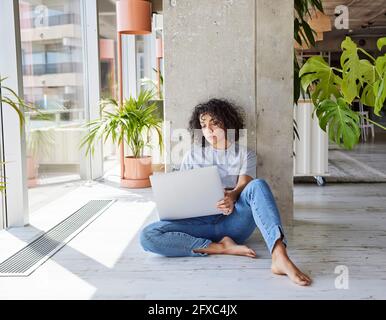 Lockige Frau, die auf dem Boden vor der Säule in der Wohnung sitzt Stockfoto