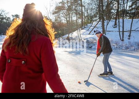 Älterer Mann spielt Eishockey mit Frau im Winter auf Schnee Stockfoto