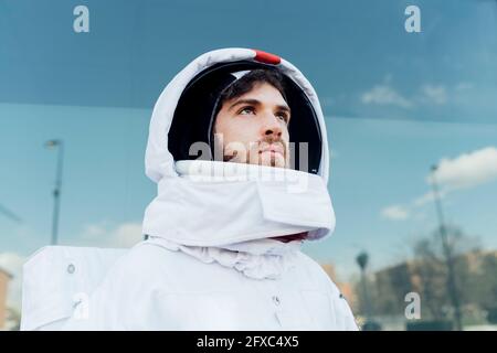 Nachdenklicher männlicher Astronaut im Weltraumanzug, der in der Stadt wegschaut Stockfoto