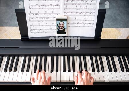 Frau mit mittlerem Erwachsenen, die zu Hause Klavier spielt, während sie einen Videoanruf führt Stockfoto