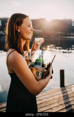 Glückliche, schöne Frau, die während des Sonnenuntergangs Eiskübel auf dem Steg trug Stockfoto