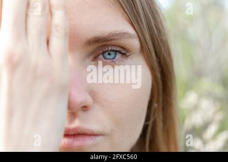 Junge Frau starrt, während sie das Gesicht mit der Hand bedeckt Stockfoto