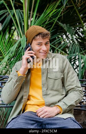 Lächelnder Mann mit Strickmütze, der im Park auf dem Handy spricht Stockfoto