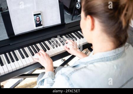 Frau mit mittlerem Erwachsenen, die zu Hause Klavier übt, auf Videoanruf Stockfoto