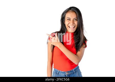 Junge lächelnde, dunkelhaarige Lateinerin zeigt auf einem rein weißen Hintergrund auf ihre rechte Seite. Stockfoto