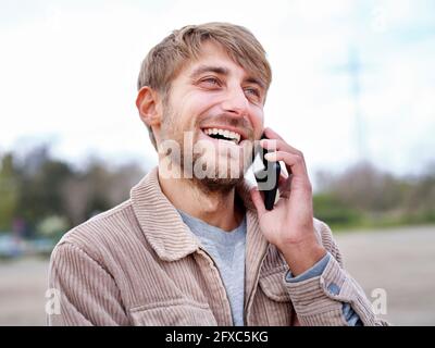 Glücklicher bärtiger Mann, der beim Telefonieren auf dem Smartphone wegschaute Stockfoto
