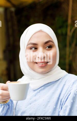 Junge Frau schaut weg, während sie die Kaffeetasse im Straßencafé hält Stockfoto