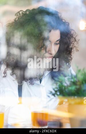 Junge Frau mit lockigen Haaren im Restaurant durch Glas gesehen Stockfoto