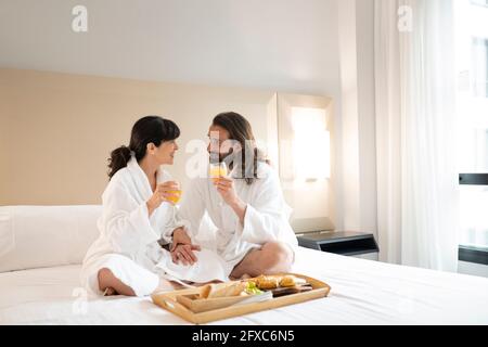 Ein Paar in Bademänteln, das Saft auf dem Bett in der Hotelsuite trank Stockfoto