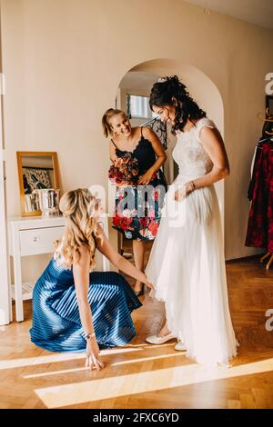 Glückliche Freundinnen bereiten Braut im häuslichen Zimmer Stockfoto