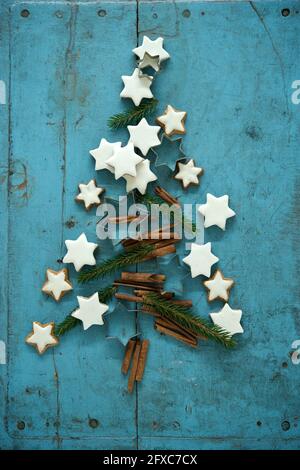 Weihnachts-Zimt-sternförmige Kekse zusammen mit Zimt- und Nadelzweigen in Weihnachtsbaum auf blauem rustikalem Holzhintergrund angeordnet Stockfoto