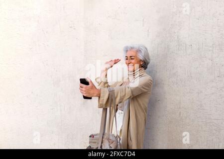 Glückliche reife Frau mit Einkaufstasche winkende Hand während Videoanruf Stockfoto
