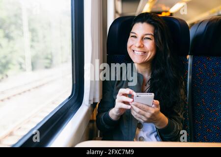 Frau mit Mobiltelefon schaute durch das Fenster, während sie im Zug saß Stockfoto