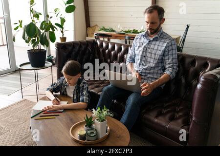 Vater mit Laptop, während Sohn zu Hause zeichnen Stockfoto