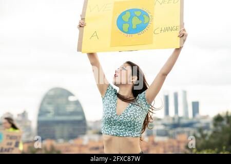 Junge Frau schaut nach oben, während sie das Banner unter dem Himmel hält Stockfoto