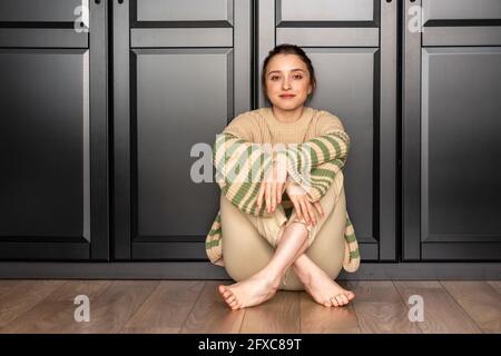 Frau mit Pullover sitzt zu Hause auf dem Boden Stockfoto