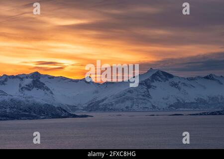 Norwegen, Tromso, Kvaloya, dramatischer Himmel über dem verschneiten Berg Senja Island bei Sonnenuntergang von der Insel Kvaloya aus gesehen Stockfoto