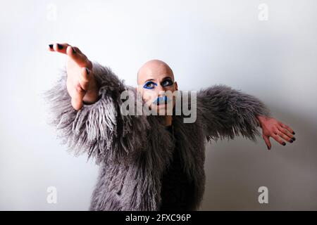 Mann mit Make-up auf dem Gesicht, der wegschaut und die Arme auf weißem Hintergrund ausstreckt Stockfoto