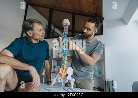 Männlicher Physiotherapeut erklärt dem Patienten in der Praxis das Wirbelsäulenmodell Stockfoto