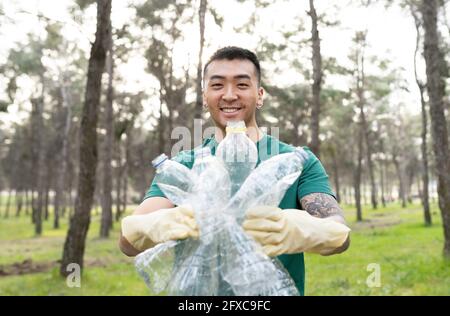 Umweltschützer lächelt, während er Plastikflaschen im Wald hält Stockfoto