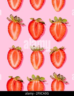Muster aus Reihen von frischen halbierten Erdbeeren, die auf rosa Hintergrund liegen Stockfoto