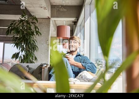 Ein hübscher Mann lächelt, während er auf dem Sofa im Loft sitzt Stockfoto