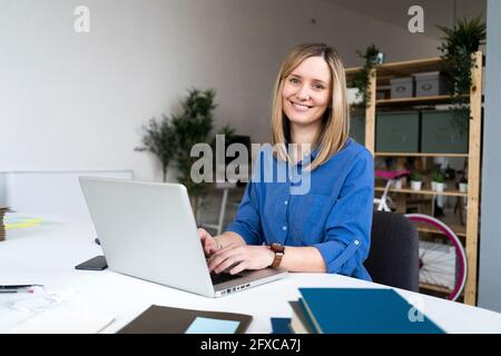 Lächelnde Geschäftsfrau, die im Büro auf dem Laptop tippt Stockfoto