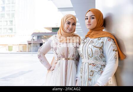 Schöne Freunde in Hijabs und Kleid stehen zusammen an der Wand Stockfoto