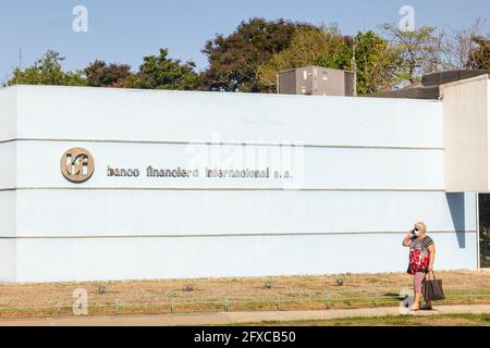 Eine ältere kubanische Frau, die mit einem Smartphone spricht und eine schützende Gesichtsmaske trägt, geht am Schild der Banco Financiero Internacional, Santiago de, vorbei Stockfoto