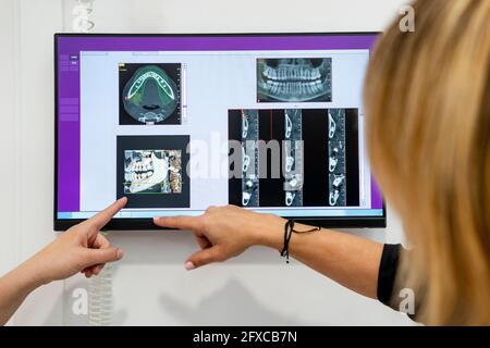 Zahnärztin und Patientin, die in der medizinischen Klinik auf ein digitales Bild auf dem Bildschirm zeigt Stockfoto