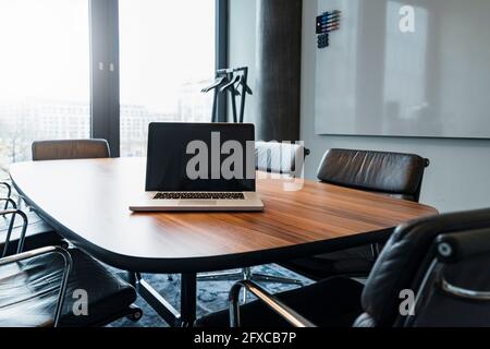 Leerer Laptop auf dem Konferenztisch inmitten von Bürostühlen Stockfoto