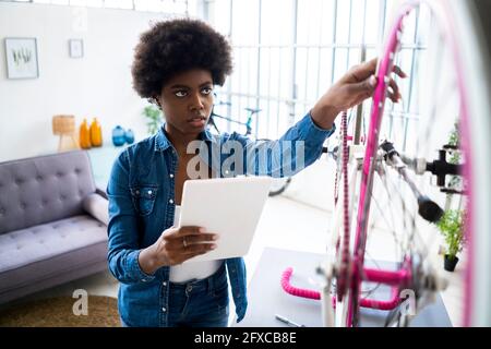 Afro-Frisur Frau mit digitalen Tablet während der Reparatur Fahrrad zu Hause Stockfoto