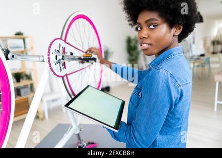Junge Frau mit digitalem Tablet Reparatur Fahrrad zu Hause Stockfoto