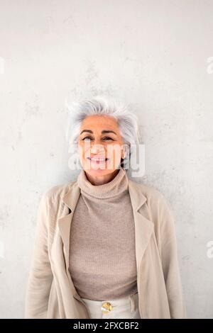 Reife Frau lächelt, während sie vor der Wand steht Stockfoto