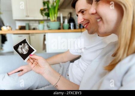 Lächelnder Ehemann und Ehefrau, die zu Hause Ultraschallbilder betrachten Stockfoto