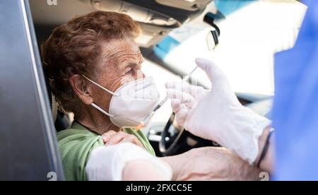 Ältere Frau, die im Auto von einer Ärztin geimpft wird Stockfoto