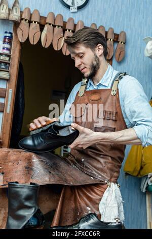 Männlicher Schuster in Schürze Polierschuh mit Pinsel in der Werkstatt Stockfoto
