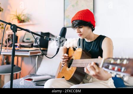 Weibliche Gitarristin trägt Strickmütze, während sie Gitarre im Studio spielt Stockfoto
